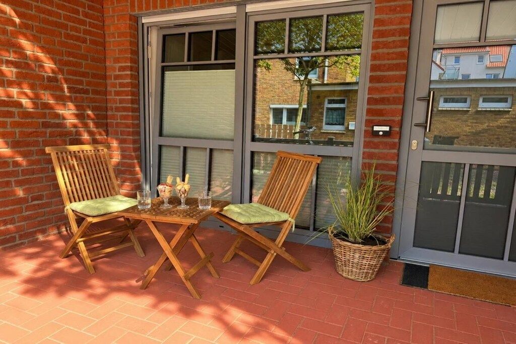 A patio with two wooden chairs and a table, a potted plant, and a sliding glass door.