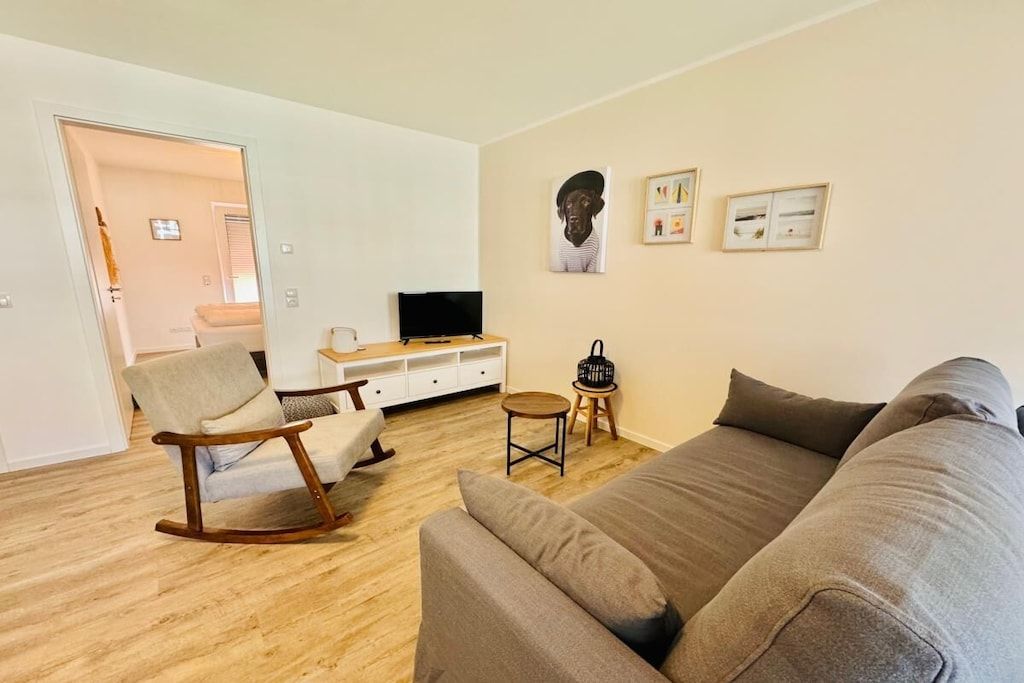 Sala de estar com um sofá, uma poltrona de balanço, uma televisão e uma pequena mesa com uma bolsa.