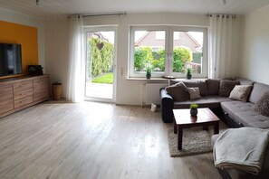 A modern living room with a sofa, a coffee table, and a TV on a wooden cabinet. - Holiday home in Hooksiel with swimming pool (Hooksiel)