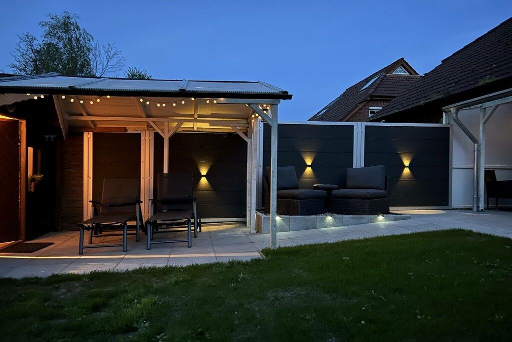 A covered outdoor seating area with chairs and tables, a garage door, and a well-lit pathway.