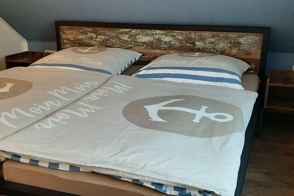 A bed with a headboard featuring a vintage cityscape print, two pillows with a circular design, and a bedspread with a nautical theme.