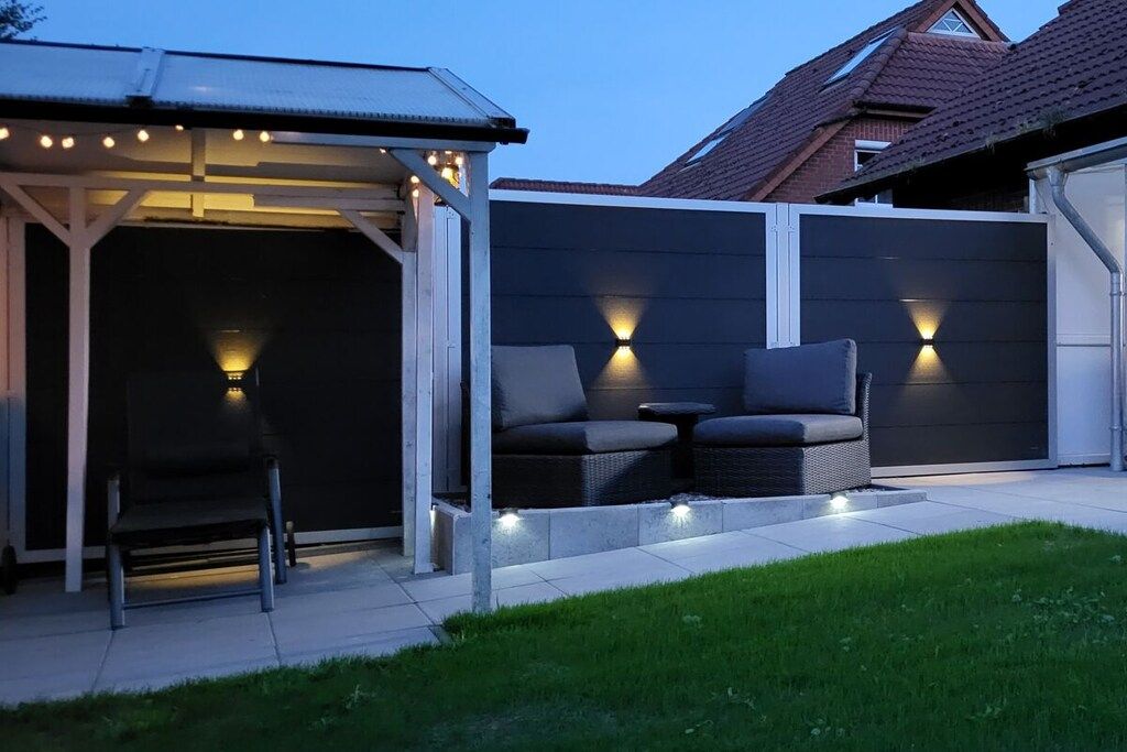 Een overdekt terras met een stoel en twee banken, een patio met betegelde vloer en een gazon.