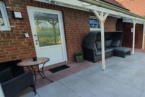 A patio with a covered seating area, a table, and a door. - Holiday home in Hooksiel with swimming pool (Hooksiel)