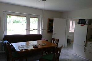 Un coin repas avec une table en bois, des chaises et un canapé. On trouve un four à micro-ondes sur un meuble, et une porte qui donne sur une autre pièce.