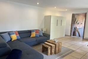 Ein modernes Wohnzimmer mit einem grauen Sofa, bunten Kissen, einem Holztisch und einem weißen Kleiderschrank.
