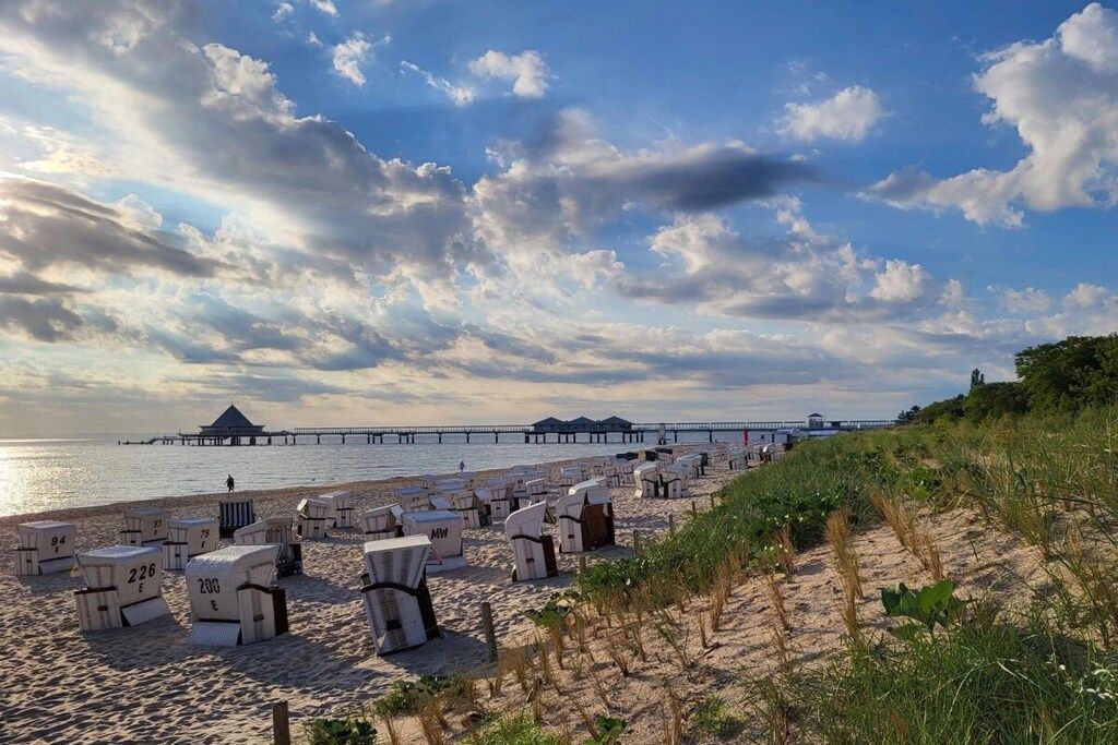 Ein Strand mit Liegestühlen und Sonnenschirmen, ein Steg im Hintergrund und ein klarer Himmel.