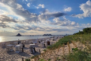 Ein Strand mit Liegestühlen und Sonnenschirmen, ein Steg im Hintergrund und ein klarer Himmel.