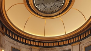 Un lobby espacioso con techo circular, una escalera central y vista hacia un comedor.