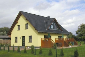 A two-story house with a sloped roof, a wooden deck, and a fenced yard. - 2 in the house by the water (Ziemitz)