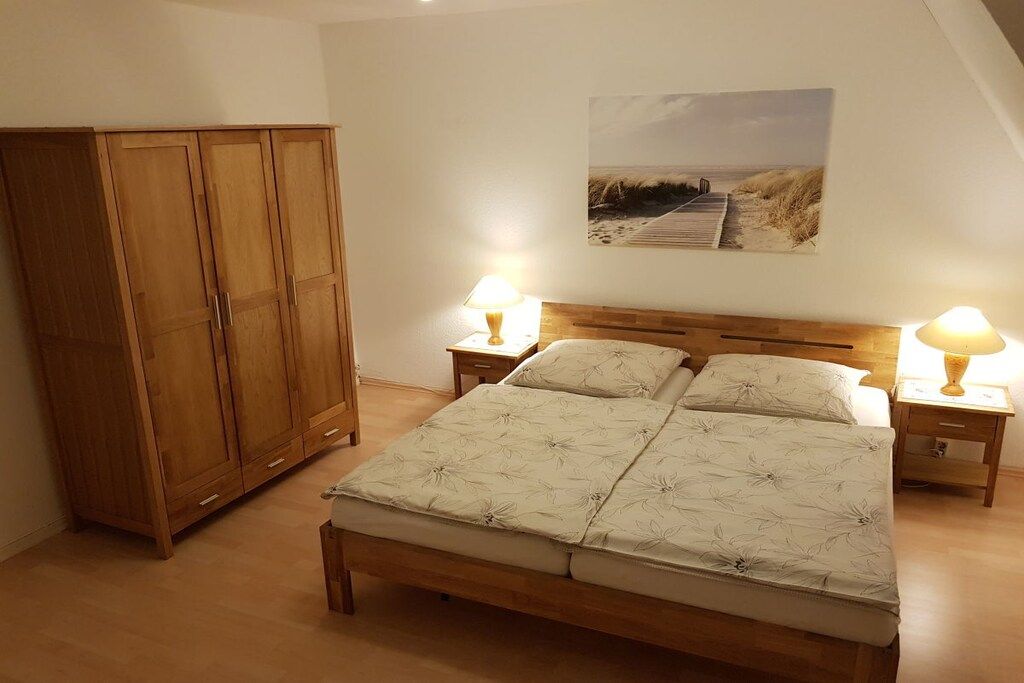 Une chambre à coucher avec un lit en bois, deux tables de chevet avec des lampes, une armoire en bois et un tableau mural sur le thème de la plage.