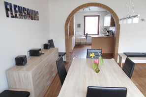 A dining area with a long table, chairs, a vase with flowers, and a kitchen visible through an archway. - Holiday apartment with 2 bedrooms (Flensburg)