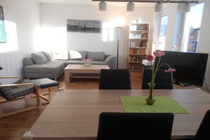 Un saló modern amb un sofà, una taula de centre i una taula de dinar amb cadires. Hi ha una estanteria i un televisor de pantalla plana.