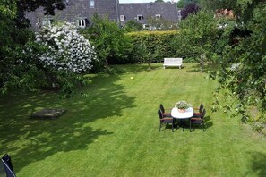 A well-maintained garden with a round table and chairs, surrounded by lush greenery and a hedge. - Holiday apartment with 2 bedrooms (Flensburg)