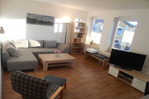 A living room with a sofa, a coffee table, a television, and a bookshelf. - Holiday apartment with 2 bedrooms (Flensburg)