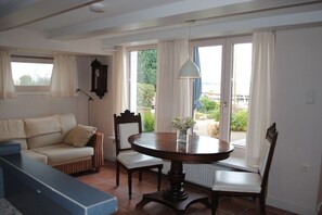 A room with a round wooden table, two chairs, a sofa, and a window with curtains. - Holiday apartment with 1 bedroom (Stexwig)