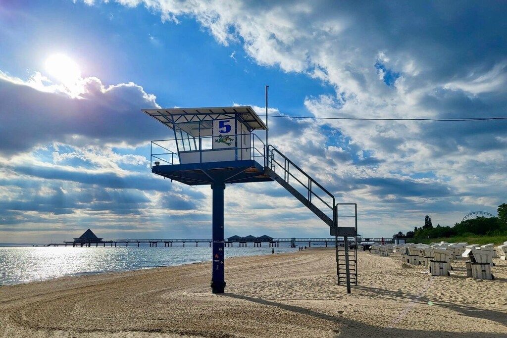A lifeguard tower with a number '5' on a beach with a pier in the background.