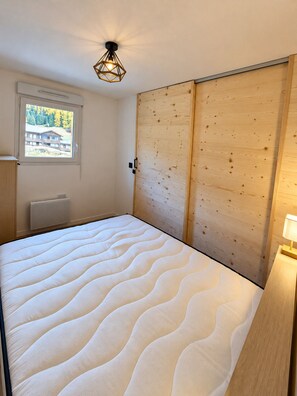 A bedroom with a bed, a window, a radiator, and a wooden wardrobe. - Apartment with a balcony and a heated swimming pool (Allos)