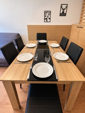 Une table à manger dressée pour quatre personnes, avec des chaises, un set de table noir et un tableau accroché au mur.