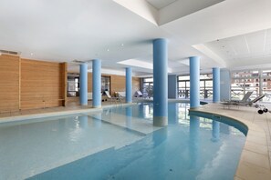 An indoor swimming pool with blue columns, lounge chairs, and a wooden wall. - Apartment with a balcony and a heated swimming pool (Allos)
