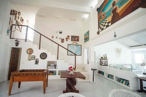 A spacious living area with a wooden foosball table, a staircase, and a large abstract painting.