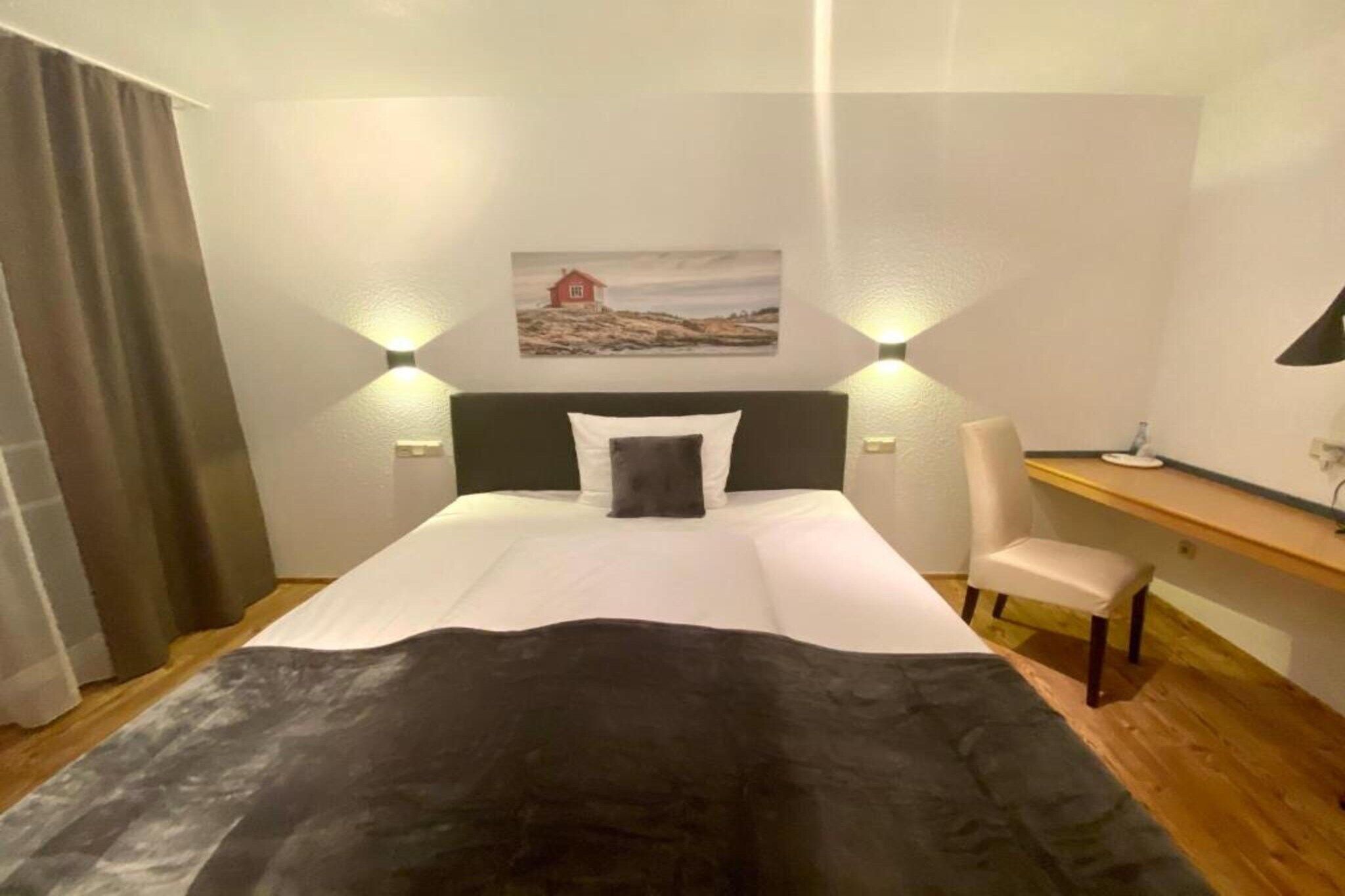 A hotel room with a bed, a desk, a chair, and a painting on the wall.