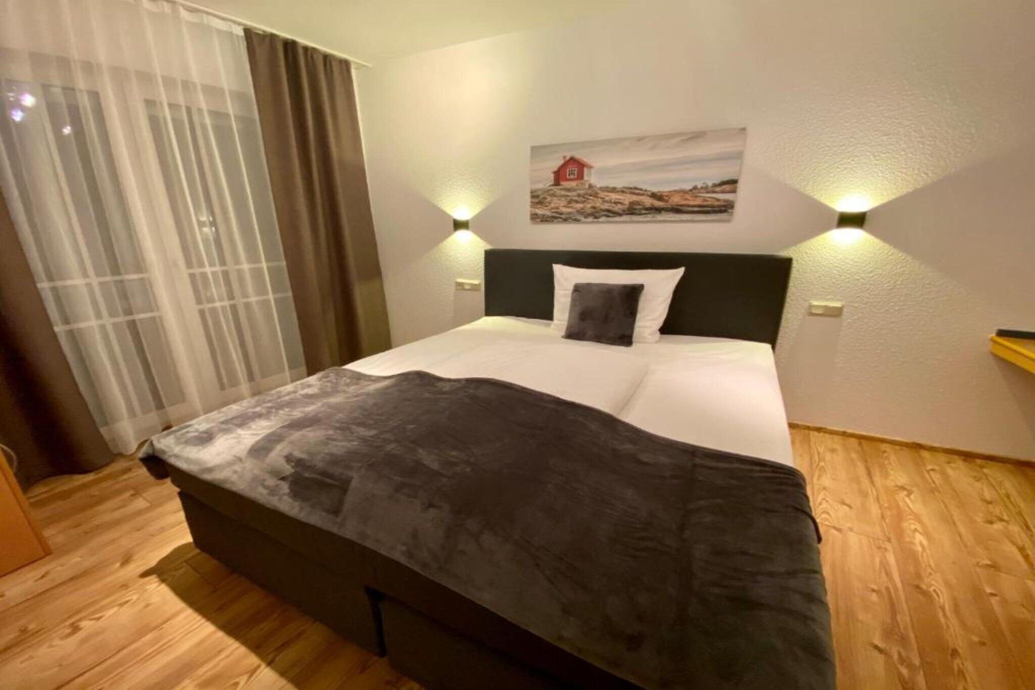 A hotel room with a bed, curtains, a painting, and a wooden floor.