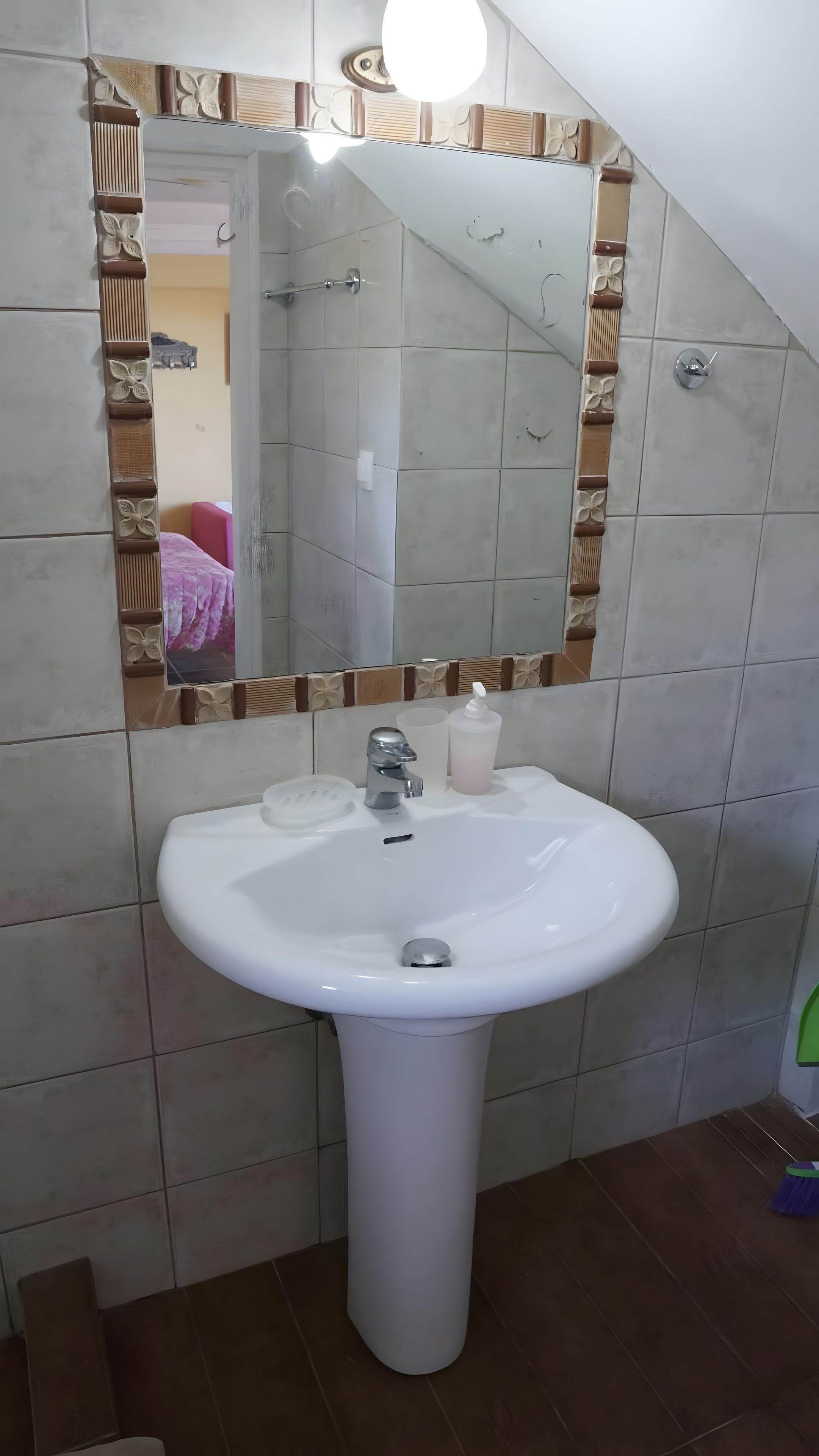 A bathroom with a white sink, a mirror with decorative tiles, and a shower area.