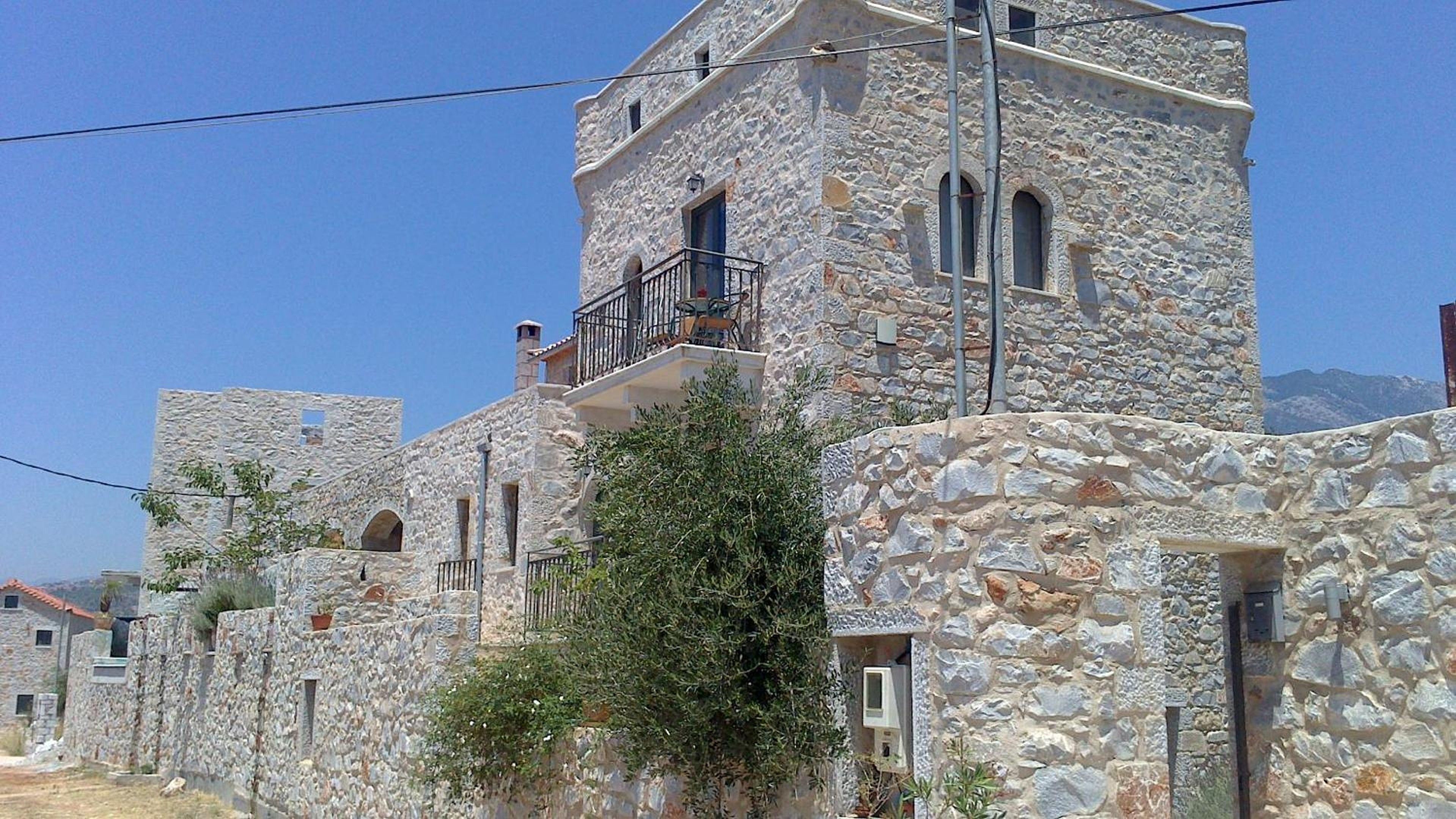 Un edificio in pietra con un balcone, diverse finestre e montagne sullo sfondo.