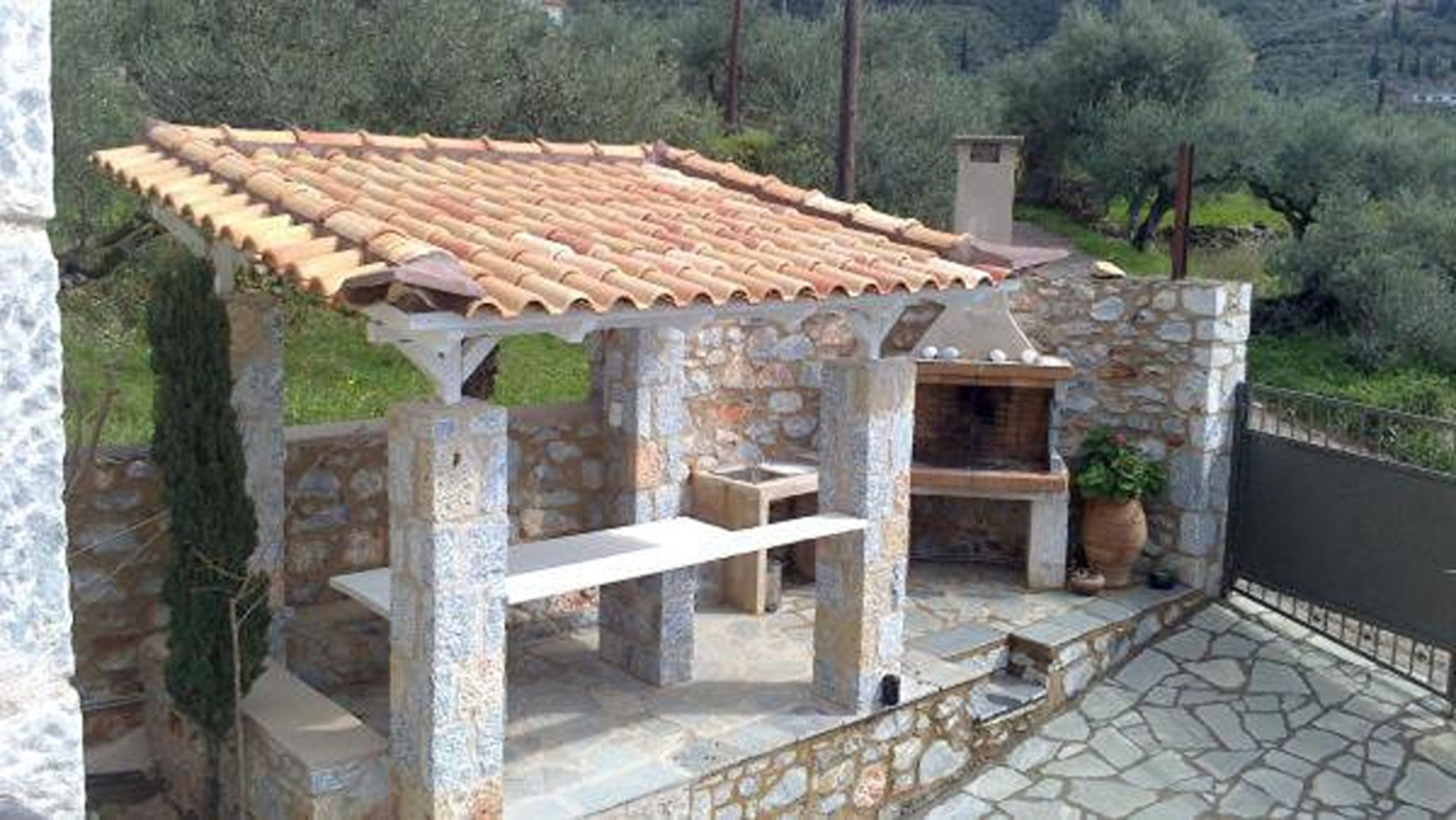 Eine Terrasse aus Stein mit geflastertem Dach, einem eingebauten Grill und einer Steinsitzbank.