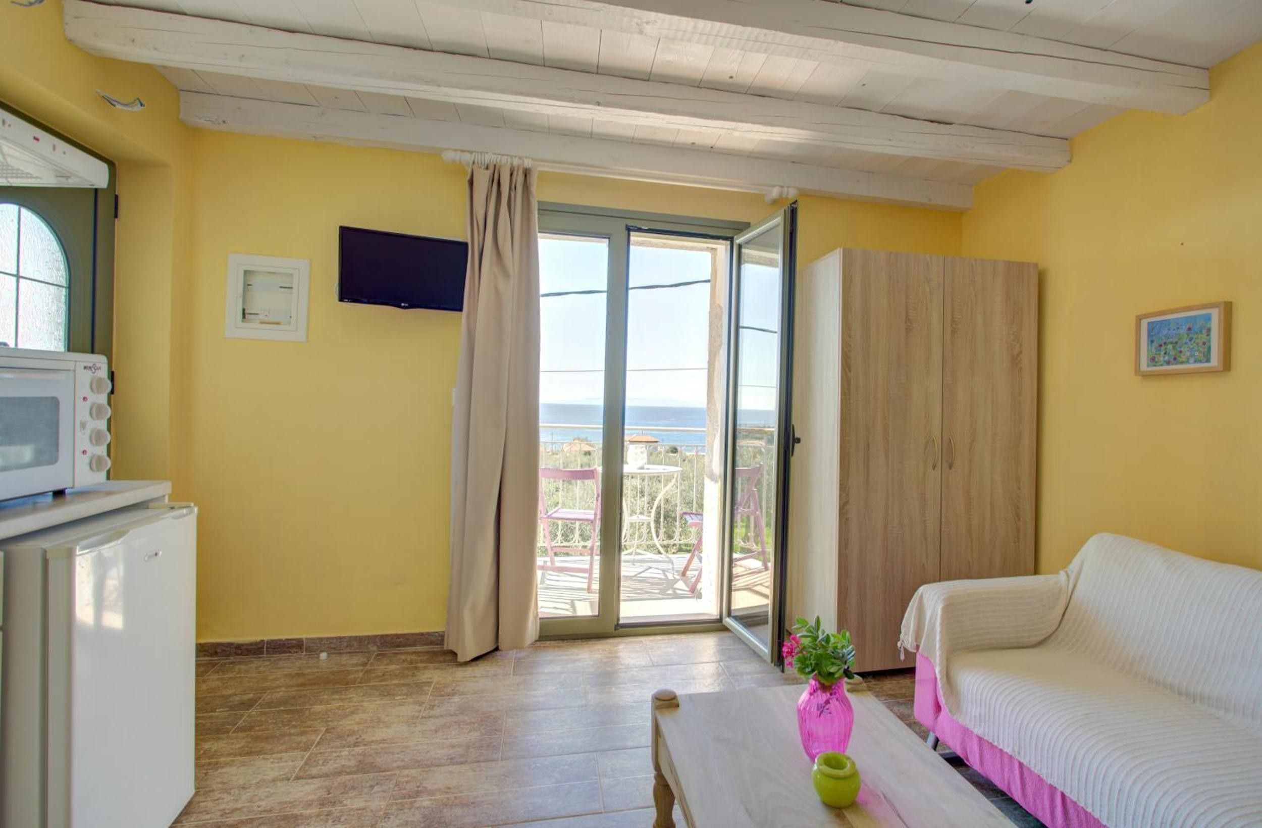 A room with a sliding glass door to a balcony, a white sofa, a small table with a vase, and a wooden wardrobe.