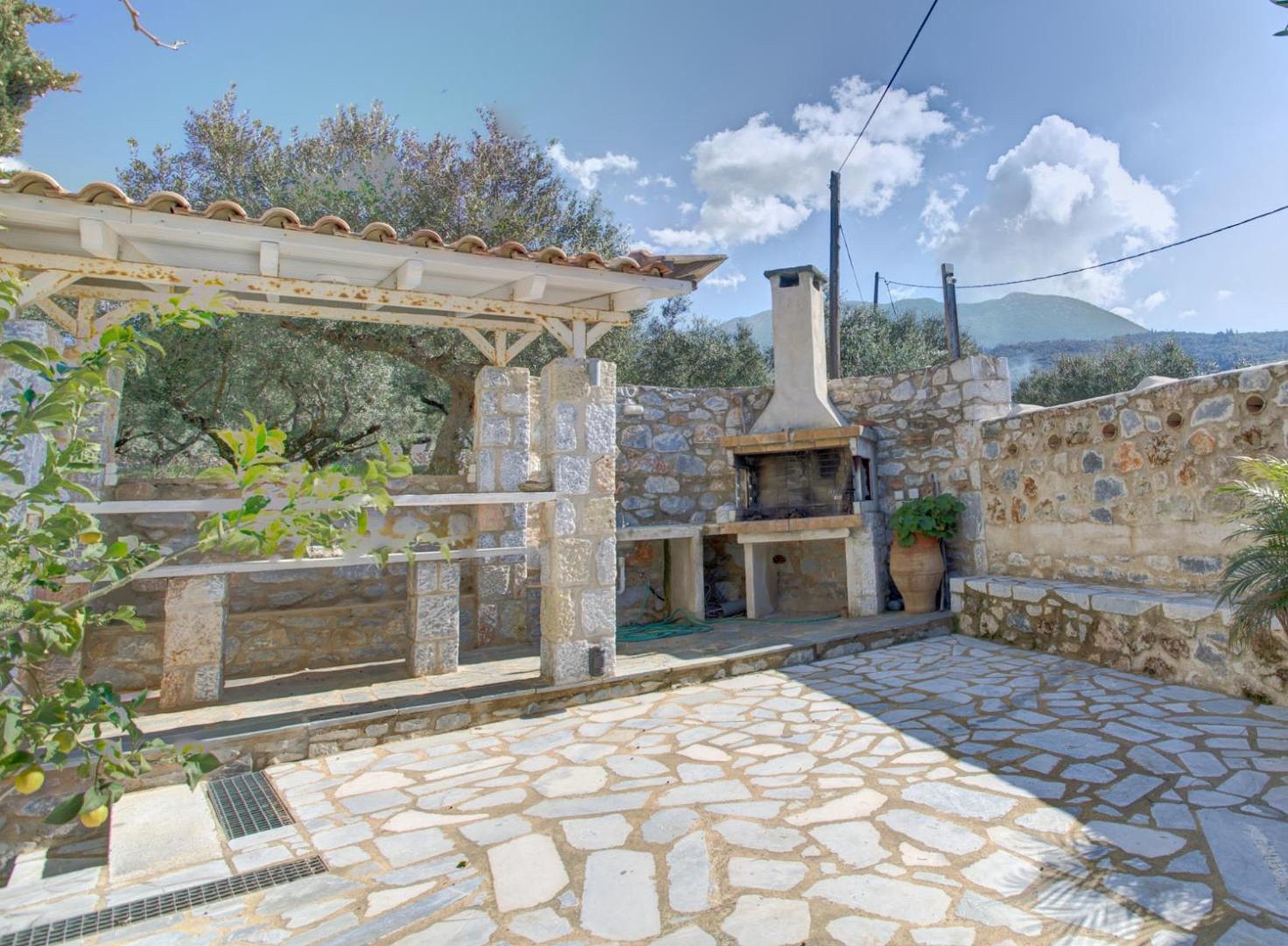 Un patio in pietra con zona barbecue integrata, una pergola e un muro in pietra.