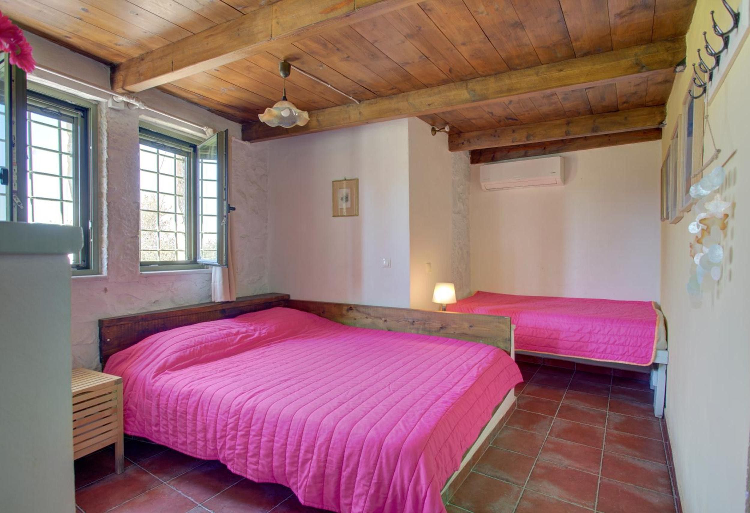 Ein Schlafzimmer mit zwei Betten, Holzbalkendecke, einem Fenster und einer Wand-Klimaanlage.