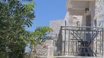 Un edificio de piedra con un balcón y una escalera que conduce a la entrada, bajo un cielo azul despejado.