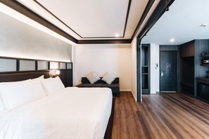 A hotel room with a large bed, a sofa, a desk, and a wardrobe.