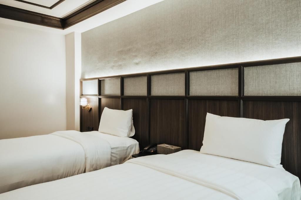 Une chambre d’hôtel avec deux lits, une tête de lit en bois et une table de chevet avec une lampe.