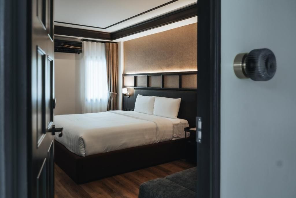 A hotel room with a bed, a nightstand, a lamp, and a window with curtains.