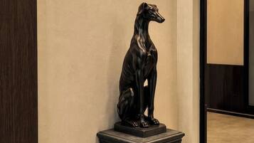A black dog statue on a pedestal in a hallway with a wall-mounted light fixture.