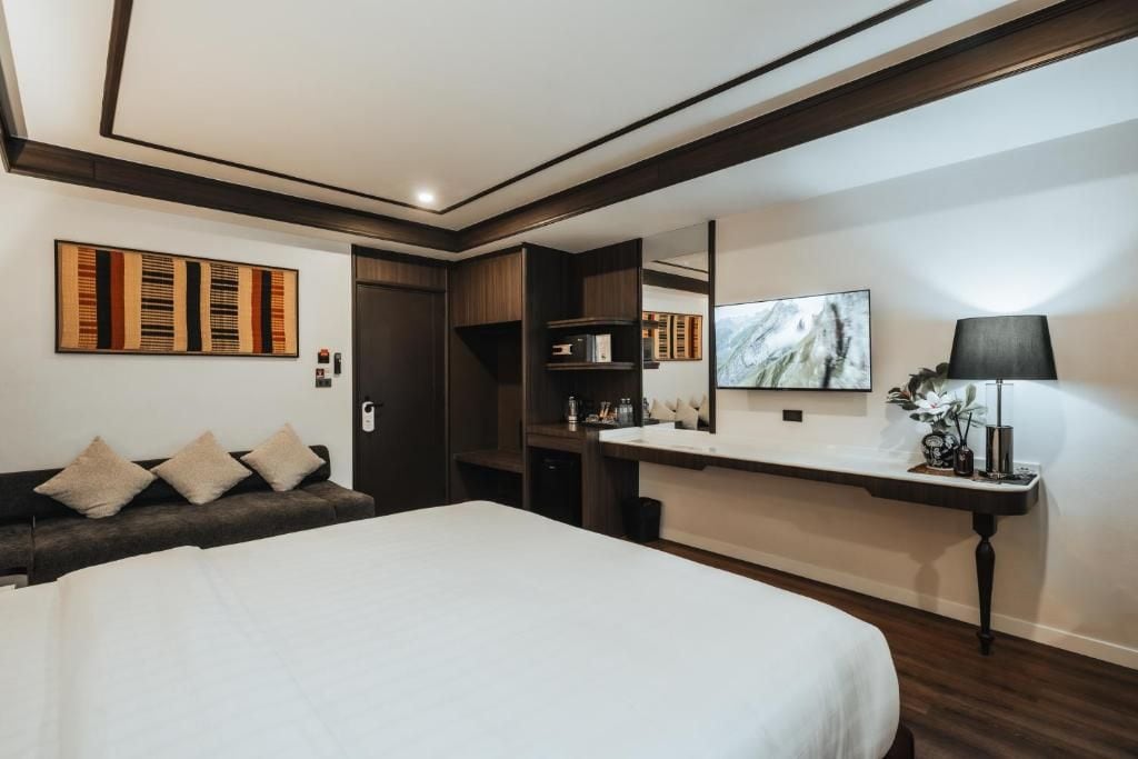 A modern hotel room with a large bed, a desk with a mirror, and a sofa with cushions.