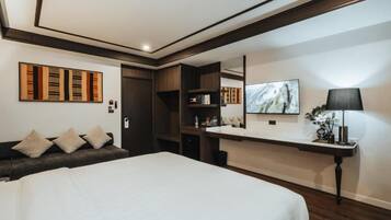 A modern hotel room with a large bed, a desk with a mirror, and a sofa with cushions.