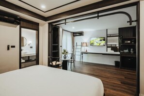 A hotel room with a bed, a desk, a chair, a TV, and a kitchenette.