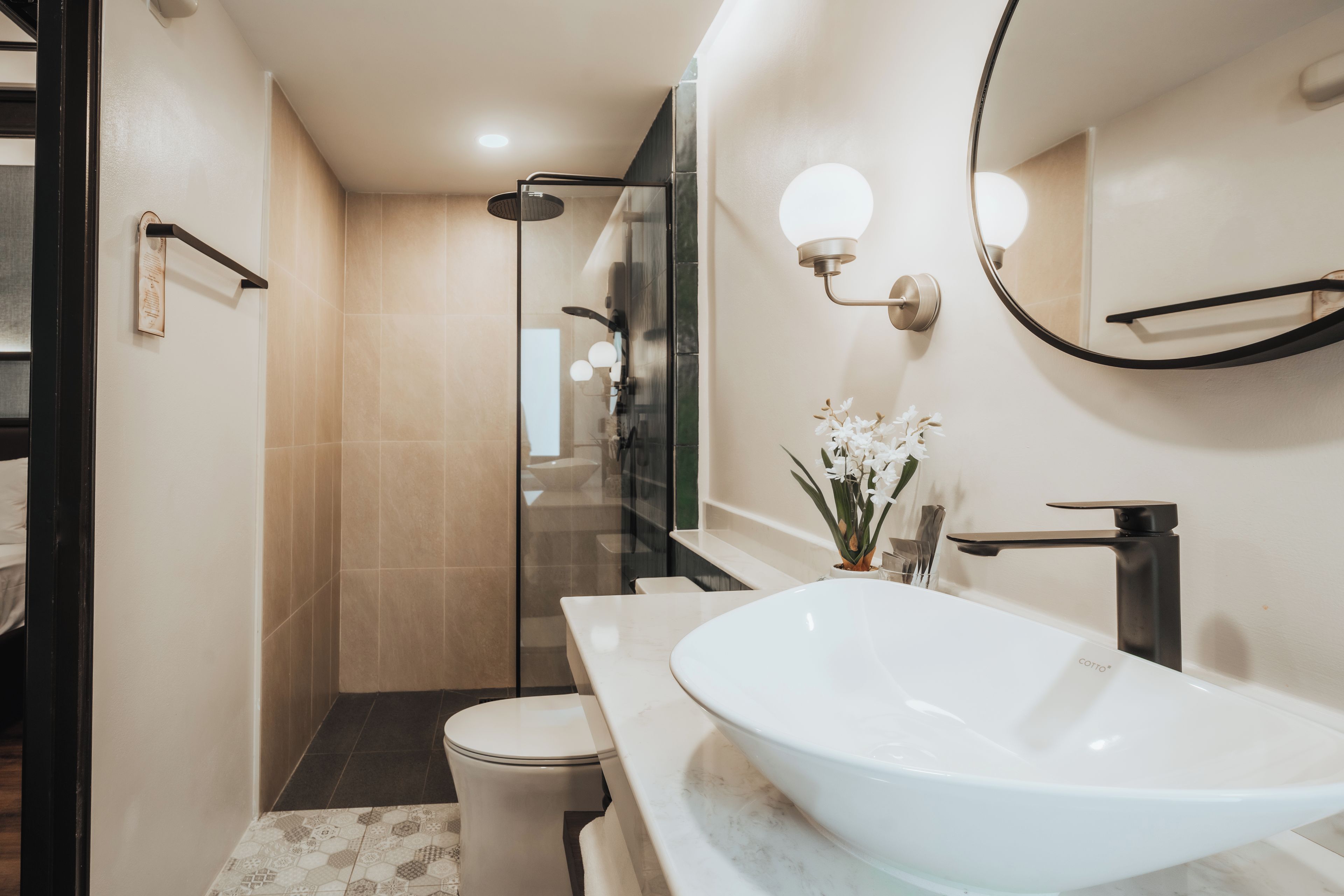 A modern bathroom with a large white sink, a glass shower enclosure, and a mirror with wall-mounted lights.