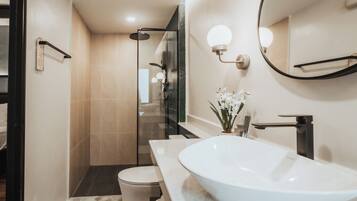 A modern bathroom with a large white sink, a glass shower enclosure, and a mirror with wall-mounted lights.