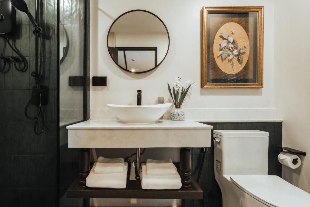 Une salle de bain avec un lavabo blanc, un miroir rond, une œuvre d’art encadrée et des toilettes.