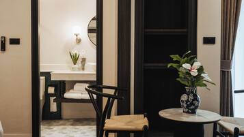 Habitación de hotel con una mesa redonda, una silla, un jarrón pequeño con flores, un espejo y una toalla en la pared.