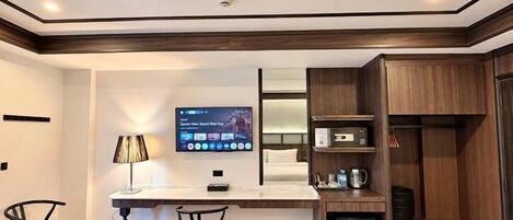 A modern kitchen with a flat-screen TV, wooden cabinets, and a small refrigerator.