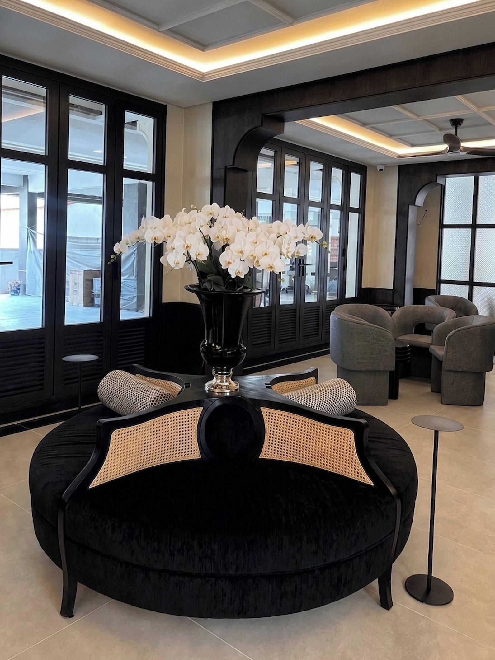 Ein stilvoller Aufenthaltsraum mit einer schwarzen Couch, einer Vase mit weißen Blumen und Blick durch große Fenster.