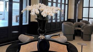 Un salon moderne avec un canapé noir, un vase de fleurs blanches et une vue dégagée grâce à de grandes fenêtres.
