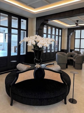 Ein stilvoller Aufenthaltsraum mit einer schwarzen Couch, einer Vase mit weißen Blumen und Blick durch große Fenster.