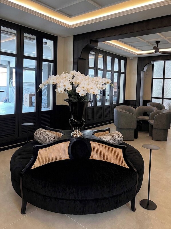 A modern lounge area with a black sofa, a vase of white flowers, and a view through large windows.