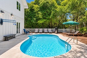 Ein Swimmingpool mit weißem Zaun, Liegestühlen und einem Sonnenschirm.
